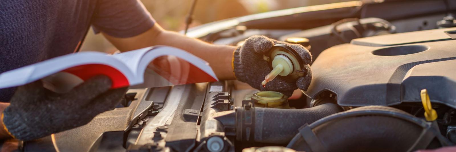 Anweisungs- und Nachweissysteme Mechaniker haelt ein Buch in seiner rechten Hand und macht den Oeldeckel eines Autos mit der linken Hand auf